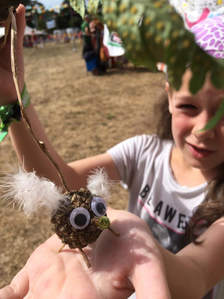 child holding up a bug she made out of forest materials at a festival