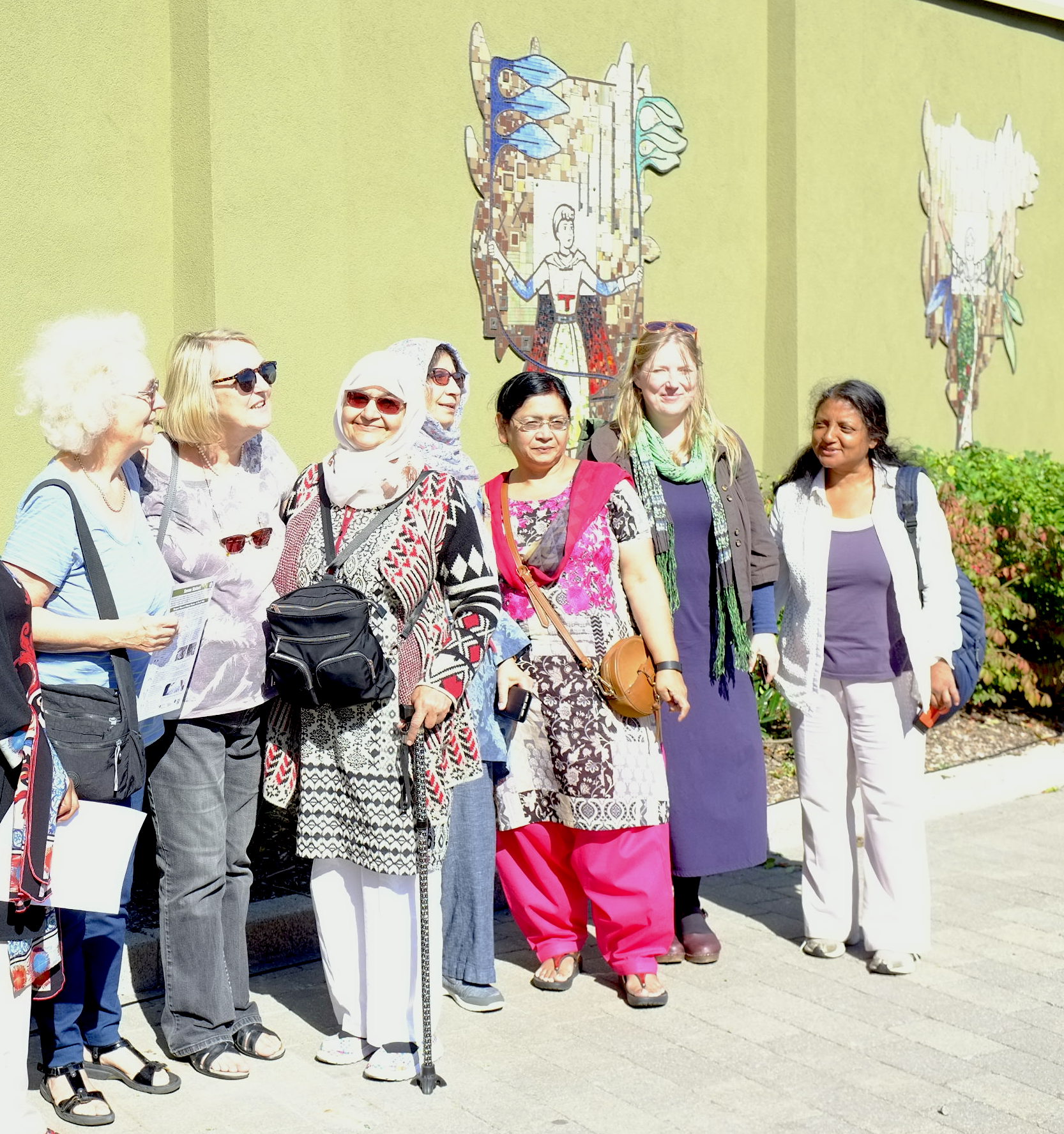 multi cultural group of ladies who helped make the mosaic behind them