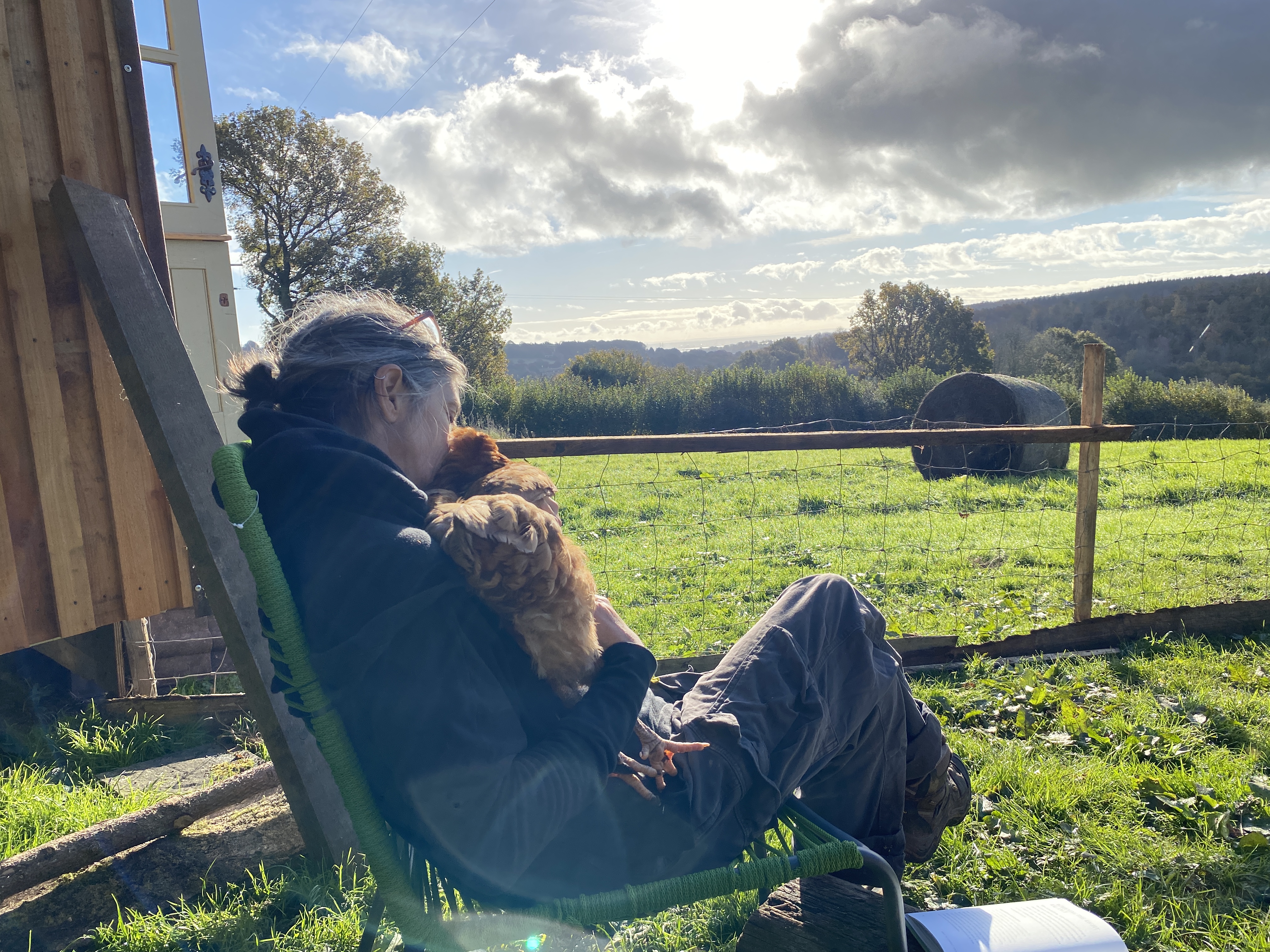 woman sat on a chair outside cwtshing a chicken