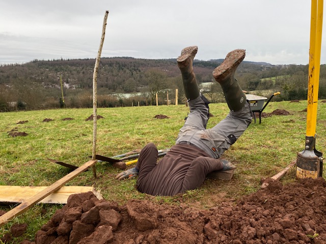 Man pretending to fall head first down a hole in a field he has dug